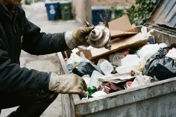 A person wearing gloves and safety glasses sorting through trash, finding a repairable lamp